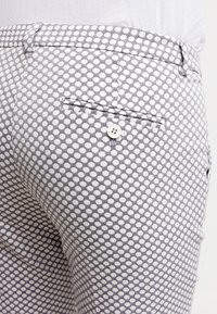 Zbliżenie na szare spodnie w biały w kropki, z tylną kieszenią z pojedynczym białym guzikiem i szlufkami na pasek.