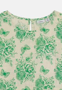 Abito floreale verde caratterizzato da un tessuto testurizzato in bianco sporco con motivi di rose, farfalle e fiori. Dettaglio con apertura a chiave sulla schiena e scollatura rotonda.