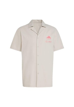 Krátký rukáv košile na knoflíky ze světle béžové tkaniny. Na levé části hrudi se nacházejí růžové loga Adidas a Mercedes. Standardní design límce.