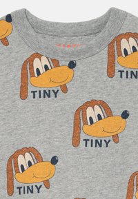 T-shirt grigia con volti di cani cartoon ripetuti; presenta accenti arancioni e marroni con la parola "TINY" in grassetto nero sotto ogni volto.