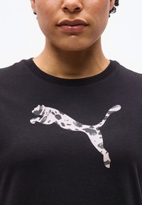 Κοντινό πλάνο ενός ατόμου που φοράει μαύρο πουκάμισο με λογότυπο ενός γάτου που πηδάει, με λευκό και μαύρο πουα μοτίβο.