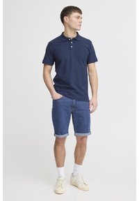 Mornarska polo majica s kratkimi rokavi in dvema gumboma na sprednji strani. Oblečena z denim kratkimi hlačami in belimi supergami. Preprost dizajn, brez vzorcev ali poudarkov.