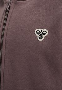 Lila zip-up sweatshirt med en texturerad tyg och en broderad svart och vit bi-logotyp på vänster bröstområde.