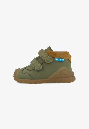 Zapatos impermeables verdes para niños pequeños con doble cierre de velcro, detalles en gamuza marrón y una suela de goma duradera con patrones antideslizantes.