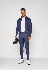 Conjunto de ciclismo azul-marinho composto por jaqueta ajustada de manga comprida e calças justas, feito de material respirável, combinado com capacete preto e sapatos brancos.