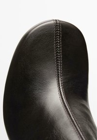 Scarpa in pelle nera con una texture liscia, caratterizzata da una cucitura prominente lungo il lato. Silhouette elegante con punta arrotondata.
