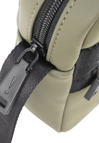 Borsa verde scuro con una superficie liscia in finta pelle, dotata di una tracolla nera texturizzata e di una cerniera metallica. Inclusi accenti di hardware notevoli.