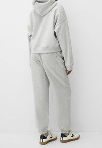 Sudadera gris corta con capucha ajustable y pantalones de chándal grises de corte suelto con puños elásticos. Las zapatillas son blancas con detalles negros.