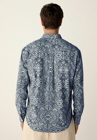 Langarmhemd mit geometrischem Blau- und Weißmuster, ausgestattet mit einem Button-Down-Kragen und abgerundetem Saum. Leichter Stoff, lässige Passform.