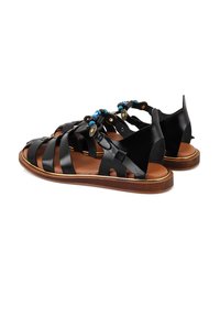Schwarze Leder-Sandalen mit geflochtenen Riemen, offenes Rückendesign, dekorative Perlen und eine braune Sohle. Strukturierte Oberflächendetails sind vorhanden.