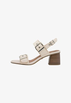 Beige heeled sandal with a glossy finish, featuring two wide straps with metallic buckles, a cushioned footbed, and a textured block heel.