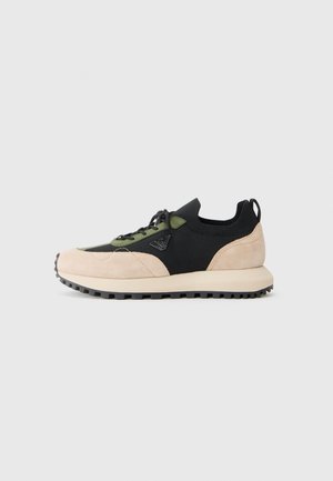 Baskets de sport rose clair et noire en matériaux en daim et en tricot. Présentent des lacets verts, une semelle texturée et un logo discret sur le côté.