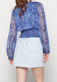 Blå blommönstrad blus med genomskinliga ärmar, cinchad midja, parat med högmidjad denimkjol med fransad kant, ljusblå färg.