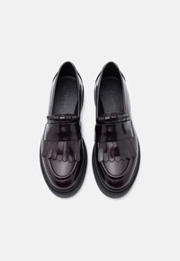 Paire de mocassins en cuir bordeaux foncé avec rabats décoratifs à franges et semelles noires, vue de dessus sur fond blanc.