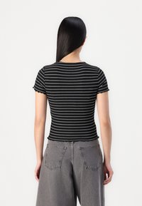 Crno-bijeli prugasti crop top s kratkim rukavima i valovitim rubom, u kombinaciji s visokim sivim trapericama koje imaju stražnje džepove.