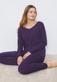 Conjunto de lounge morado que incluye una blusa de manga larga con escote en forma de barco y acentos de encaje, combinado con leggins ajustados, ambos de tejido suave.