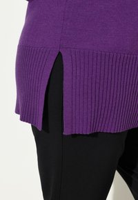 Maglione viola lavorato a maglia con orlo a coste e spacco laterale, abbinato a pantaloni neri, che mettono in risalto una combinazione di textures e un design curato.