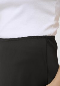 Čierne nohavice s hladkou textúrou, s vlneným okrajom v páse, kombinované s bielym rebrovaným topom.