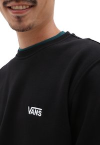Felpa nera con scollatura rotonda e dettaglio verde sul colletto. Presenta il logo "VANS" ricamato sul petto. Tessuto dalla consistenza liscia.