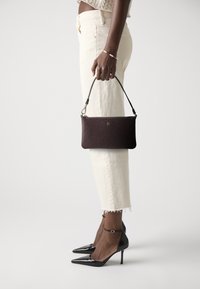 Czerwono-czarna torebka typu clutch o smukłym kształcie, ze złotymi akcentami i odpinanym paskiem, w połączeniu z białymi spodniami 3/4 i czarnymi szpilkami.