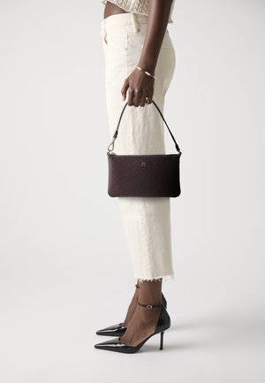Pochette à motif rouge et noir au design slim, avec des accessoires en or et une bandoulière amovible, associée à un pantalon court blanc et des talons noirs.