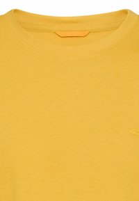 Gelbes T-Shirt mit Rundhalsausschnitt und kleinem, auf der rechten Brustseite gesticktem Logo, gefertigt aus weichem Baumwollstoff.