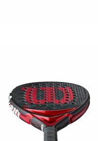 Wilson padel racket met een zwart en rood ontwerp. Gestructureerd oppervlak en perforaties voor grip, met een rood logo en een rubberen handvat.