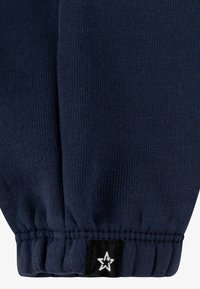 Navy blue knitted sweater cuff with a ribbed texture. Includes a black label featuring a white star design at the hem.