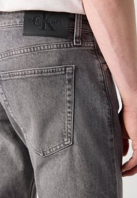 Vaqueros de mezclilla gris con una textura suave, con un parche del logo de Calvin Klein Jeans en negro y detalles en el bolsillo trasero.