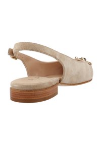 Zapato tipo slingback de ante beige con un bajo tacón de madera, que presenta una textura suave y un sencillo acento metálico en el lateral.