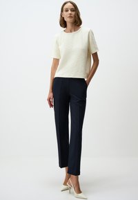 Witte, textuurrijke top met korte mouwen gecombineerd met marineblauwe, op maat gemaakte broek. Model draagt roomkleurige slingback hakken. Eenvoudige, strakke lijnen en een casual silhouet.