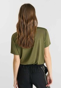 Olijfgroene, kortemd-t-shirt met een ontspannen pasvorm, gedragen met zwarte pinstripe pants. Gladde textuur, eenvoudig ontwerp, minimale details.