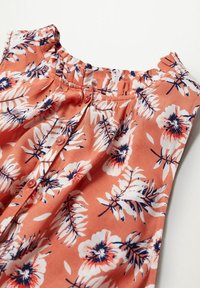 Blouse corail avec motif floral ; présente un col rond, des boutons et des détails froncés. Fabriquée en tissu léger.