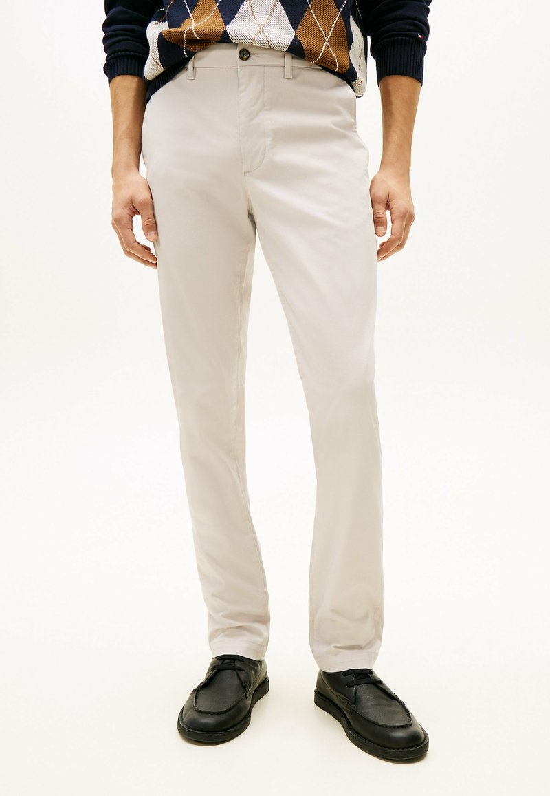 Pantalon beige clair à coupe slim, en tissu doux. Doté d'une fermeture à bouton et de poches latérales, associé à des chaussures noires.
