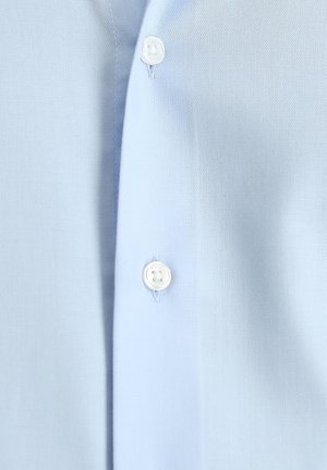 Camisa azul claro hecha de tela suave, con una tapeta de botones frontales con botones blancos. Vista en primer plano que resalta la textura y los detalles.