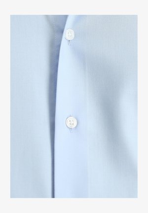 Camisa azul claro hecha de tela suave, con una tapeta de botones frontales con botones blancos. Vista en primer plano que resalta la textura y los detalles.
