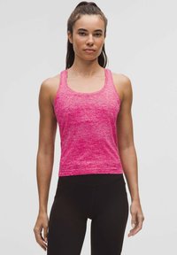 Top fucsia aderente con un motivo testurizzato, spalline larghe e scollatura rotonda. Abbinato a leggings neri, che mostrano un abbigliamento sportivo.