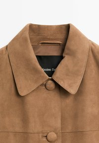 Brun ruskindsjakke med en bred krave, to runde knapper og synlige syninger. Indersiden har en sort label med "Massimo Dutti."