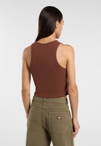 Hnědý proužkovaný crop top s kulatým výstřihem. V kombinaci s olivově zelenými kalhotami s vysokým pasem, které mají prošité kapsy a logo.