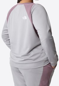 Felpa grigia chiara con texture e dettagli viola sulle spalle, logo North Face. Presenta una vestibilità comoda e polsini a costine.