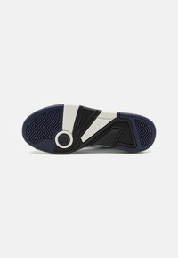 Négyzet alakú, fekete-fehér geometrikus mintázattal rendelkező gumitalpú sneaker, texturált sötétkék tapadási mintával és kör alakú díszítéssel a sarok közelében.
