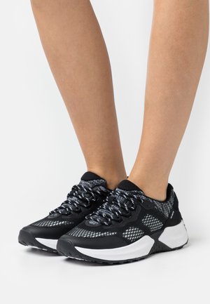 Black and white athletic shoes with a mesh upper, padded collar, textured laces, and a chunky white sole featuring a black tread.