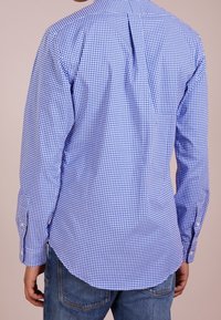 Camicia a quadri blu e bianchi con un design aderente, polsini con bottone e orlo curvo, realizzata in tessuto leggero.