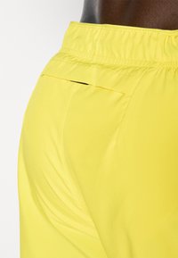 Yellow athletic shorts with an elastic waistband, featuring a side pocket and smooth, lightweight fabric texture.