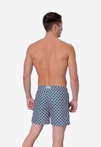 Bañadores para hombre en azul con un patrón geométrico en rosa. Cintura elástica, longitud hasta el muslo y tejido ligero. Sin detalles adicionales.