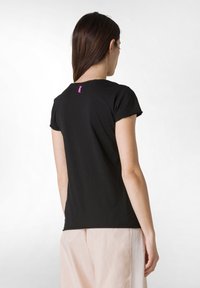 Sort kortærmet t-shirt lavet af blødt bomuld, med en lille lilla detalje nær halsudskæringen. Enkel, tætsiddende design.