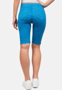 Bermuda shorts in denim blu con un design aderente, vita media e cinque tasche. Abbinati a sneakers bianche, evidenziando un look casual.