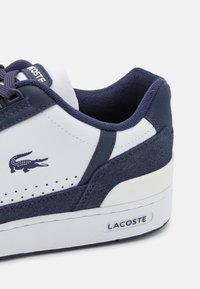 Sneaker Lacoste con una toma bianca in pelle, accenti in suede blu navy, dettagli perforati e suola in gomma, con il logo Lacoste.