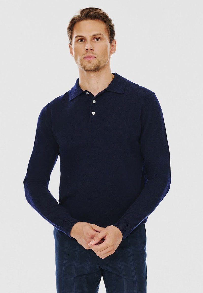 Granatowa polo z długim rękawem, z klasycznym kołnierzykiem, zapięciem na guziki i ściągaczami przy rękawach, wykonana z miękkiej dzianiny. Posiada dopasowany krój.