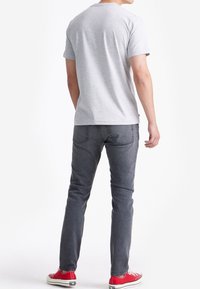 Grijze katoenen t-shirt met korte mouwen, ronde hals, gecombineerd met donkergrijze spijkerbroek en rode lage sneakers, gezien vanaf de achterkant.